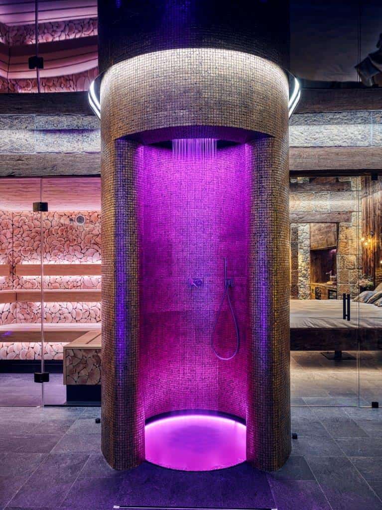 Sensory showers with coloured LED lighting and rain falling from the ceiling in a circular mosaic cubicle, next to a wood-panelled sauna.