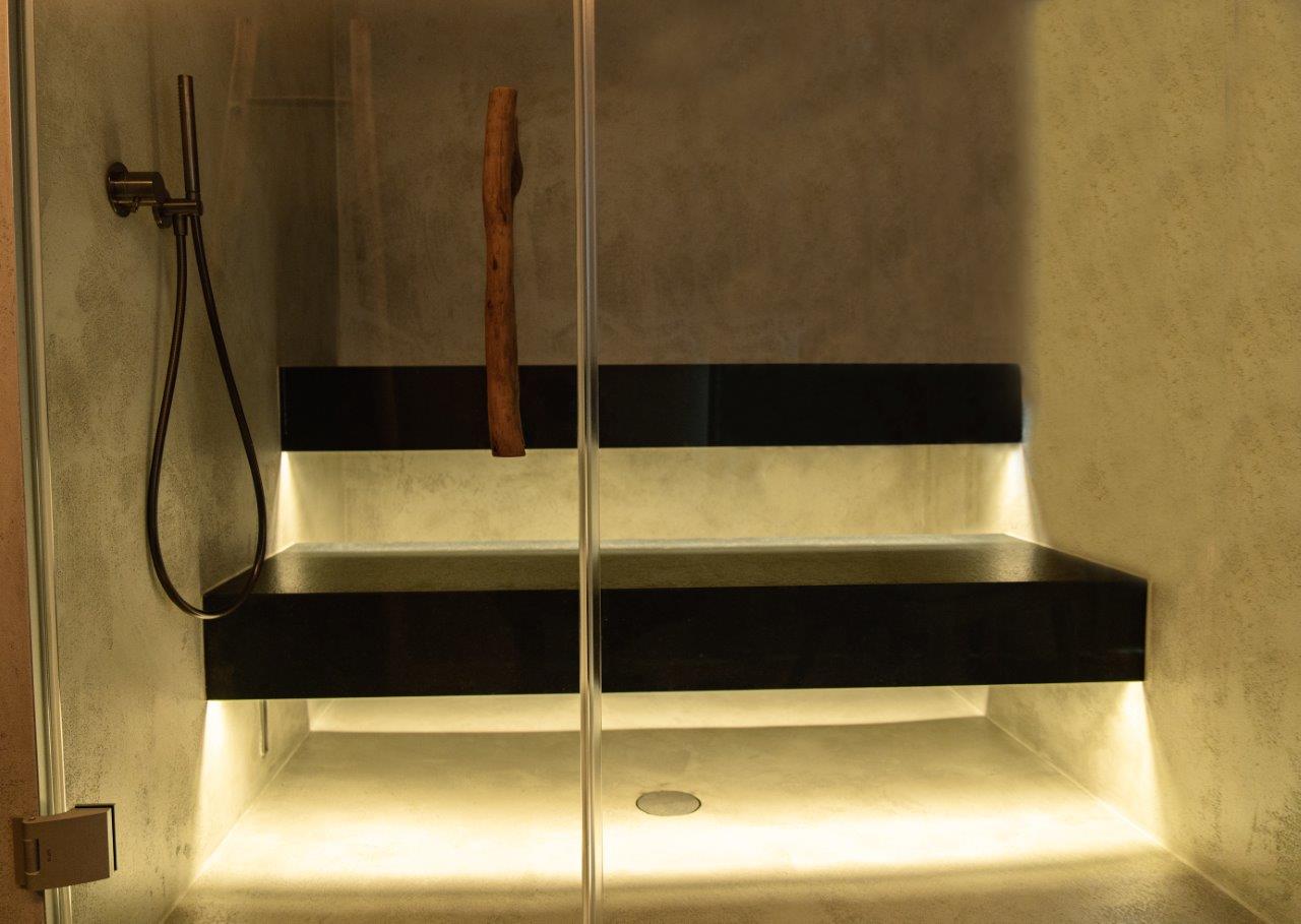 Elegantní parní sauna s černě leštěnými kamenným lavicemi, teplým LED podsvětlením, stěnami v betonu, skleněným čelem a přírodní dřevěnou větví jako designovým akcentem – parní sauna, která spojuje relaxaci a estetiku na nejvyšší úrovni. Parní sauna na míru od společnosti IMAGINOX pro hotely, spa centra a soukromé wellness prostory. Design parní sauny, parní lázeň na míru, moderní hammam, soukromá parní sauna, wellness parní lázeň – nadčasová elegance, která oslovuje všechny smysly