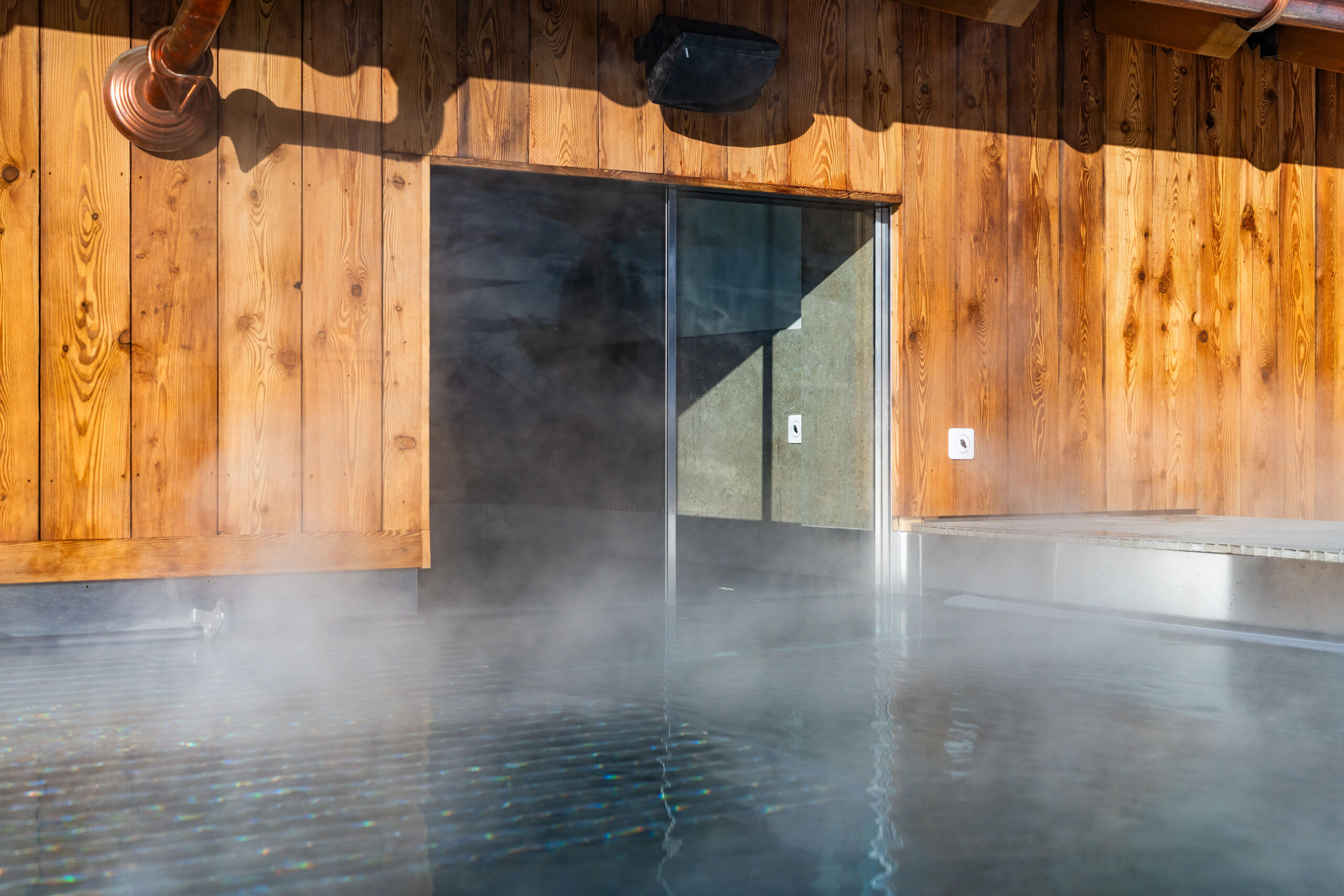 Piscina in acciaio inox riscaldata con vapore ascendente, porta scorrevole in vetro senza cornice e soffitto con travi di legno rustico – piscina in acciaio inox personalizzata di IMAGINOX per hotel, resort vacanzieri e strutture spa private. Piscina in acciaio inox interno, piscina riscaldata, piscina coperta, piscina con porta scorrevole in vetro, piscina interna in legno, piscina in acciaio inox su misura – design senza tempo, massima igiene e durabilità per progetti wellness esigenti.