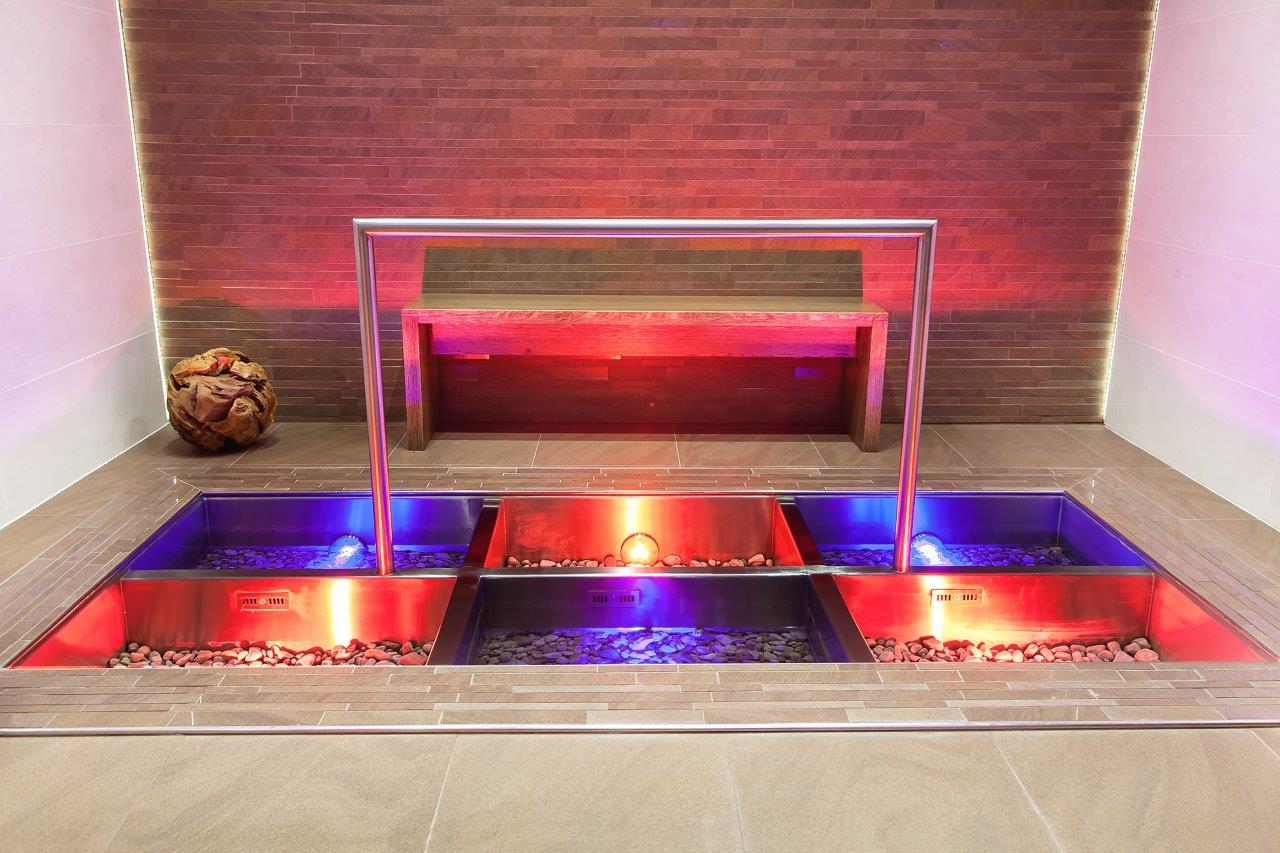 Eingelassener Kneippweg aus Edelstahl mit drei Becken, bunten Flusssteinen und dramatischer RGB-LED-Beleuchtung in Rot und Blau – hochwertige Wellness Produkte und maßgefertigte Kneipp-Anlagen von IMAGINOX für Hotels, Spa-Zentren und private Wellnessbereiche. Kneippweg nach Maß, Kneipp-Anlage, Wassertretbecken, Wellness Produkte für Hotel-Spa, Kneipptherapie, Design-Wellness – Gesundheit und Entspannung auf höchstem Niveau. 