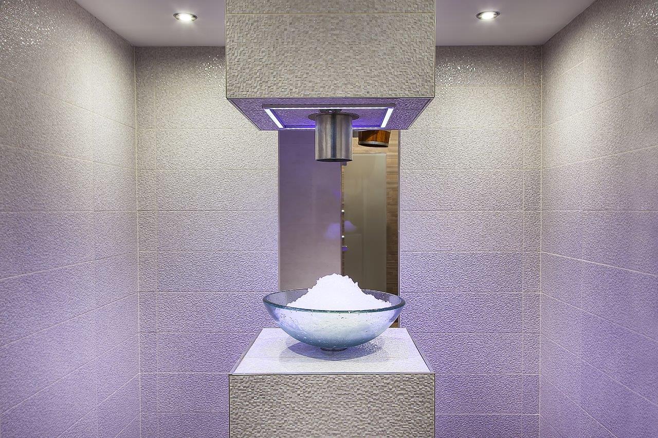 Elegante Eismaschine im Wellnessbereich mit frisch produziertem Scherbeneis in einer Glasschale, Edelstahlauslauf und stimmungsvoller violetter LED-Beleuchtung – eingebettet in eine Mosaikfliesen-Nische. Ein professioneller Eismacher ergänzt das Saunaritual perfekt: Das frische Eis dient zur intensiven Abkühlung nach dem Saunagang und unterstützt die Regeneration des Körpers. Eismaschine Wellness, Eismacher Hotel-Spa, Saunaabkühlung Eis, Wellnessprodukte Hotel, Scherbeneis Sauna – vollständige Wellness-Erfahrung auf höchstem Niveau."