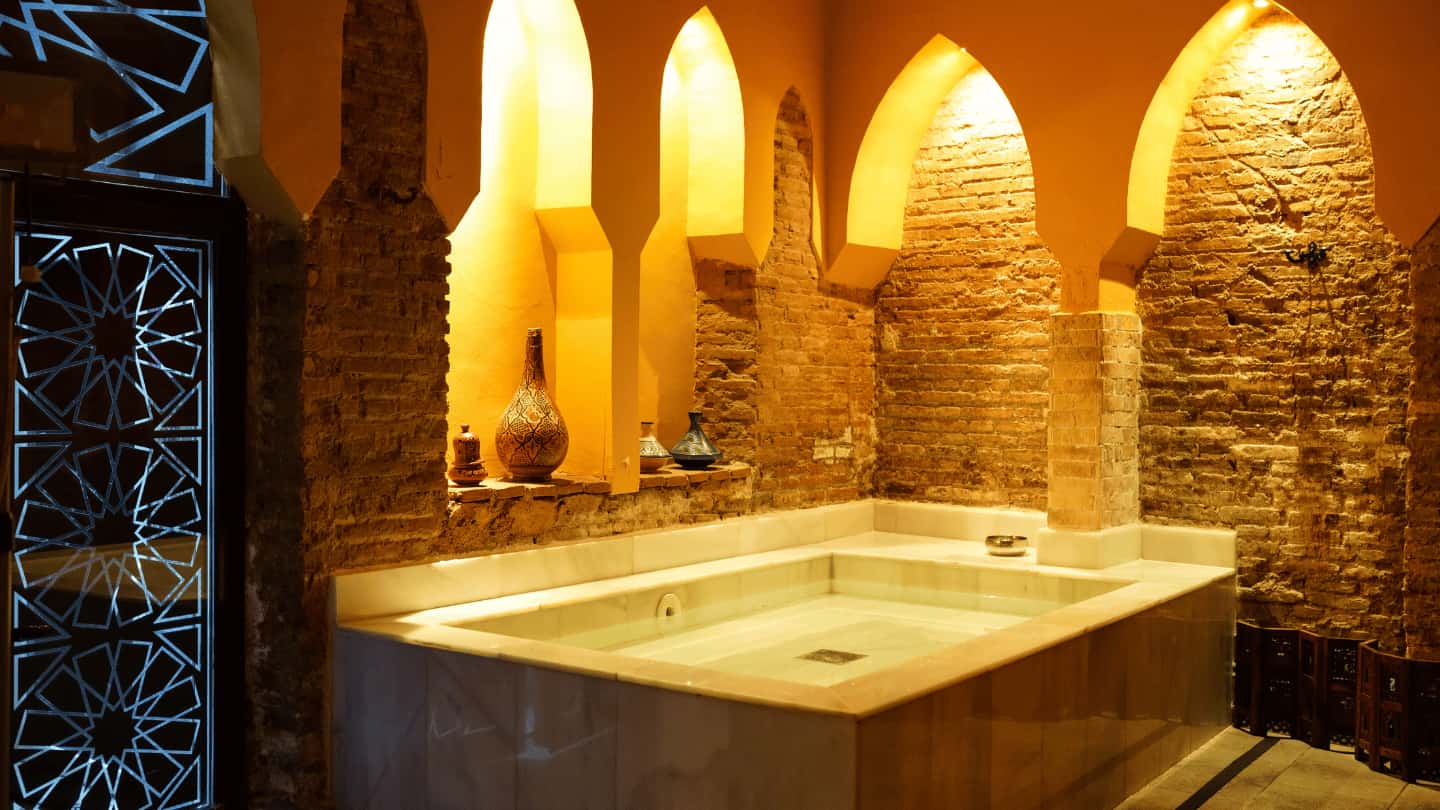 Traditionelles Hammam mit maurischen Rundbögen, warmem Licht, Natursteinwänden und zentralem Marmor-Wasserbecken – orientalisches Badehaus-Ambiente im Spa