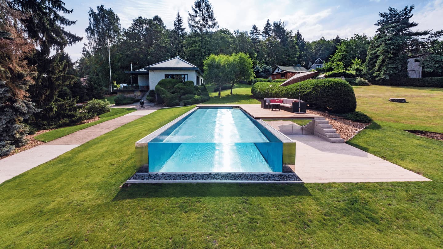 Ein maßgefertigter Edelstahlpool der Firma IMAGINOX, der an einem Hang errichtet wurde und über eine raumhohe Glaswand, türkisblaues Wasser sowie einen Panoramablick auf den Garten mit einer Terrasse zum Entspannen verfügt