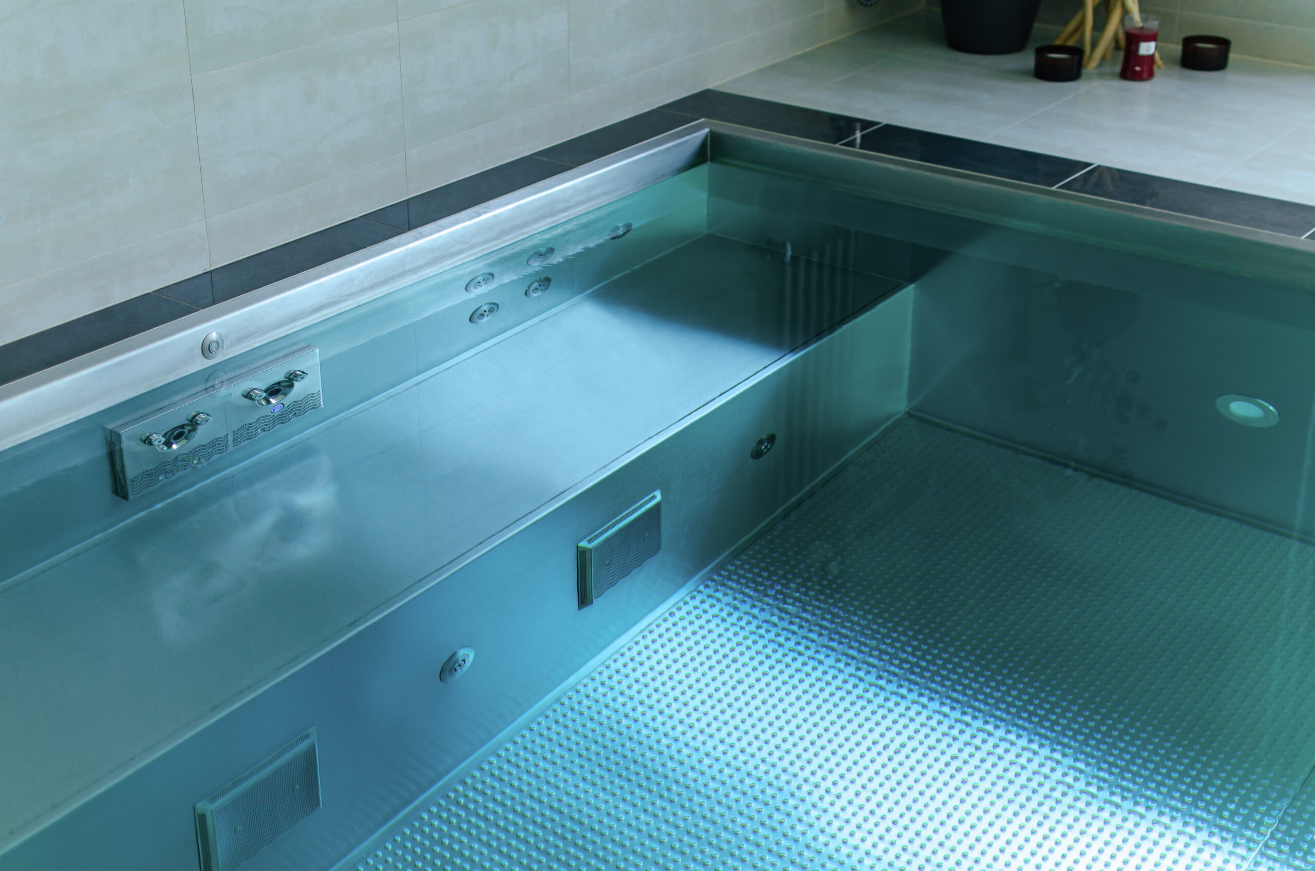 A close-up of the IMAGINOX counter-current jets in a stainless steel swimming pool with atmospheric blue LED lighting.