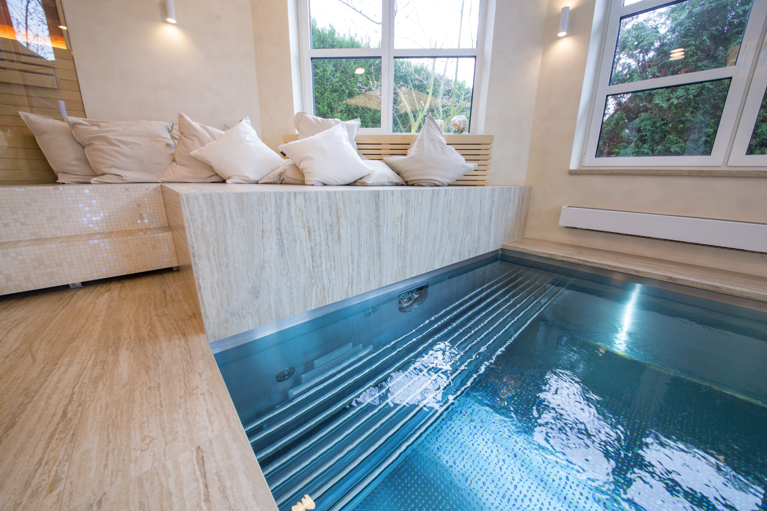 A stainless-steel counter-current pool by IMAGINOX in a cosy wellness centre, surrounded by marble cladding and soft cushions for relaxation.