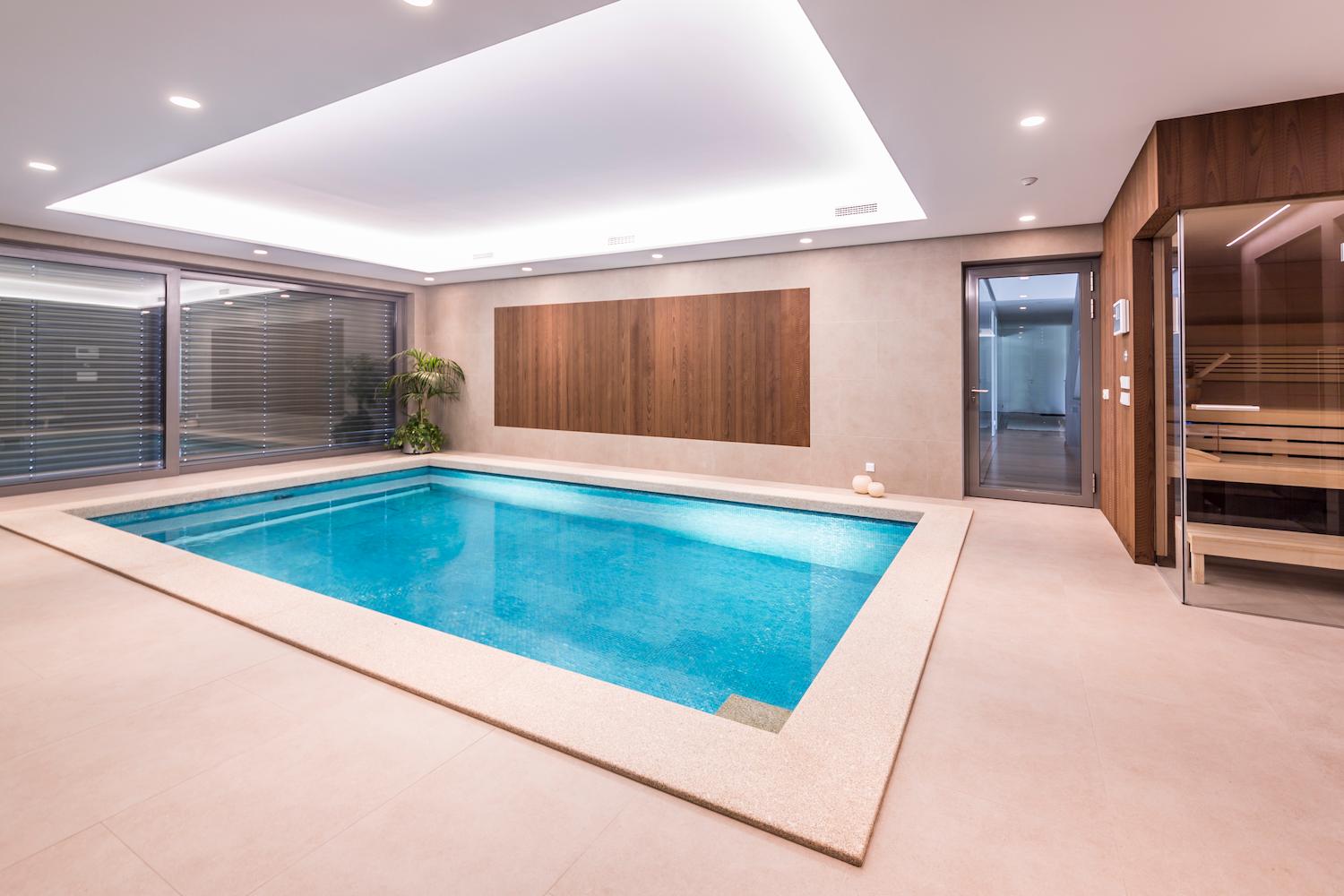Betonpool von IMAGINOX in einem modernen Wellnessbereich mit Holzakzenten und angrenzender Sauna mit Glasfront.